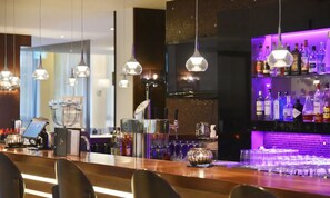 Eine moderne Bar mit hängenden Pendelleuchten, einer gut sortierten Spirituosenwand und einer Bar mit Gläsern und einer Registrierkasse.