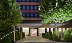 Ein Hotel Eingang mit überdachter Zugang, einem Schild mit der Aufschrift 'HOTELINGANG' und einem Gebäude im Hintergrund.