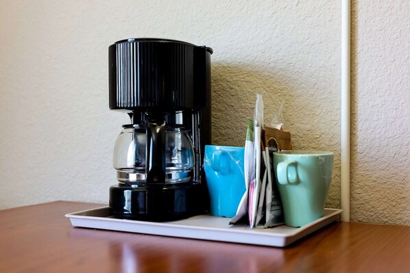Een koffiezetapparaat op een witte schaal, met een blauwe en een groene mok, en een witte muur op de achtergrond.
