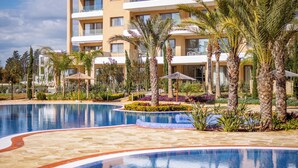 Un hôtel moderne doté d’une grande piscine, de palmiers et d’un jardin bien entretenu.