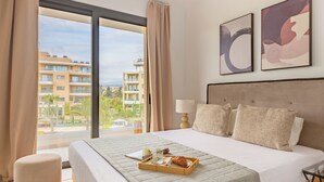 A hotel room with a large bed, a window with curtains, a bedside table with a lamp, and two abstract paintings on the wall. - Sanders Limassol Park - Chic 1 bdr apt with balcony (Trachoni Lemesou)