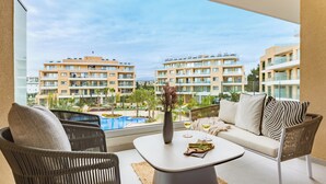A balcony with wicker chairs, a sofa, and a table with a vase and wine glasses. A pool and buildings are visible in the background. - Sanders Limassol Park - Chic 1 bdr apt with balcony (Trachoni Lemesou)
