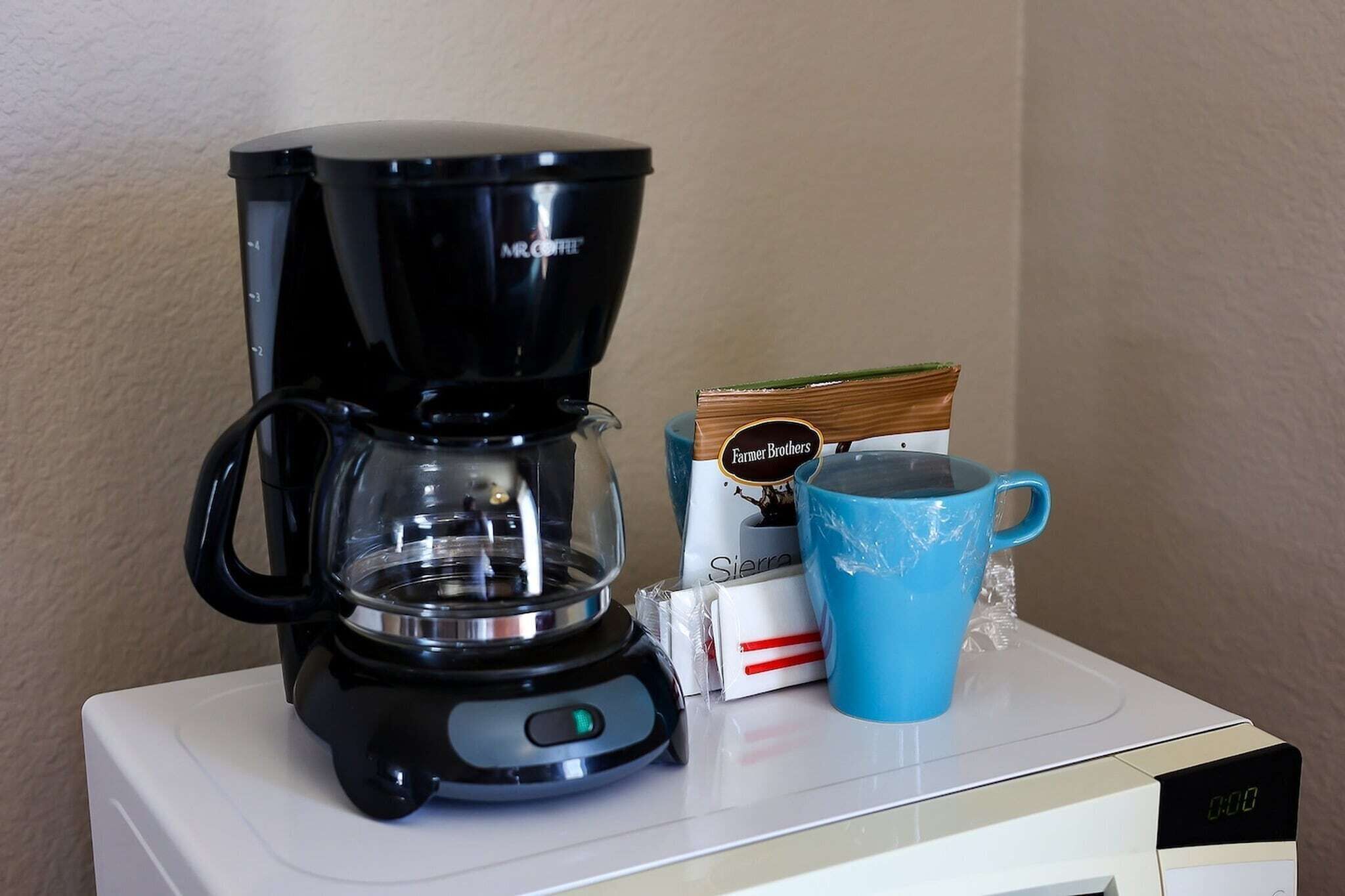 Une machine à café, une tasse bleue et une boîte de capsules de café, le tout posé sur un appareil électroménager blanc.