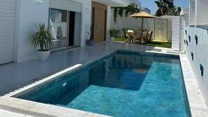 Un bâtiment moderne de couleur blanche, doté d’une piscine, de plantes en pot et de mobilier d’extérieur.