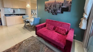 Ein modernes Wohnzimmer mit einem roten Sofa, einem Essbereich mit Tisch und Stühlen, einer Küche mit Schränken und einer Spüle sowie einem Stadtbild an der Wand.