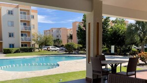 Un espacio al aire libre cubierto con piscina, mobiliario de mimbre y vistas a edificios de apartamentos.