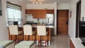Cocina compacta con una isla central, taburetes de bar, refrigerador y televisor.