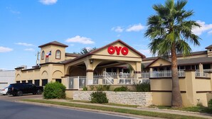 A hotel with a prominent 'OYO' sign, a palm tree, and a stone wall.