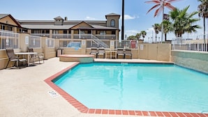 A pool area with lounge chairs, a small table, and a building with a balcony in the background.