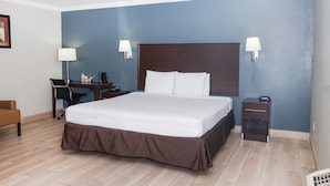 A hotel room with a bed, bedside tables, a desk with a chair, and a lamp.