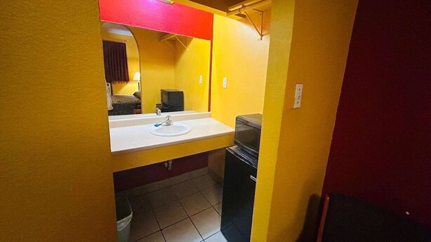 A small bathroom with a white sink, a mirror, and a black trash bin. - 2 Full Beds Non-Smoking (Sulphur LA)