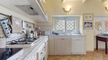 Una cocina con estufa, horno y lavavajillas, una ventana con vistas, y diversos utensilios y electrodomésticos.