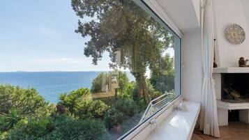 A room with a large window overlooking a coastal landscape, including trees and a view of the sea.