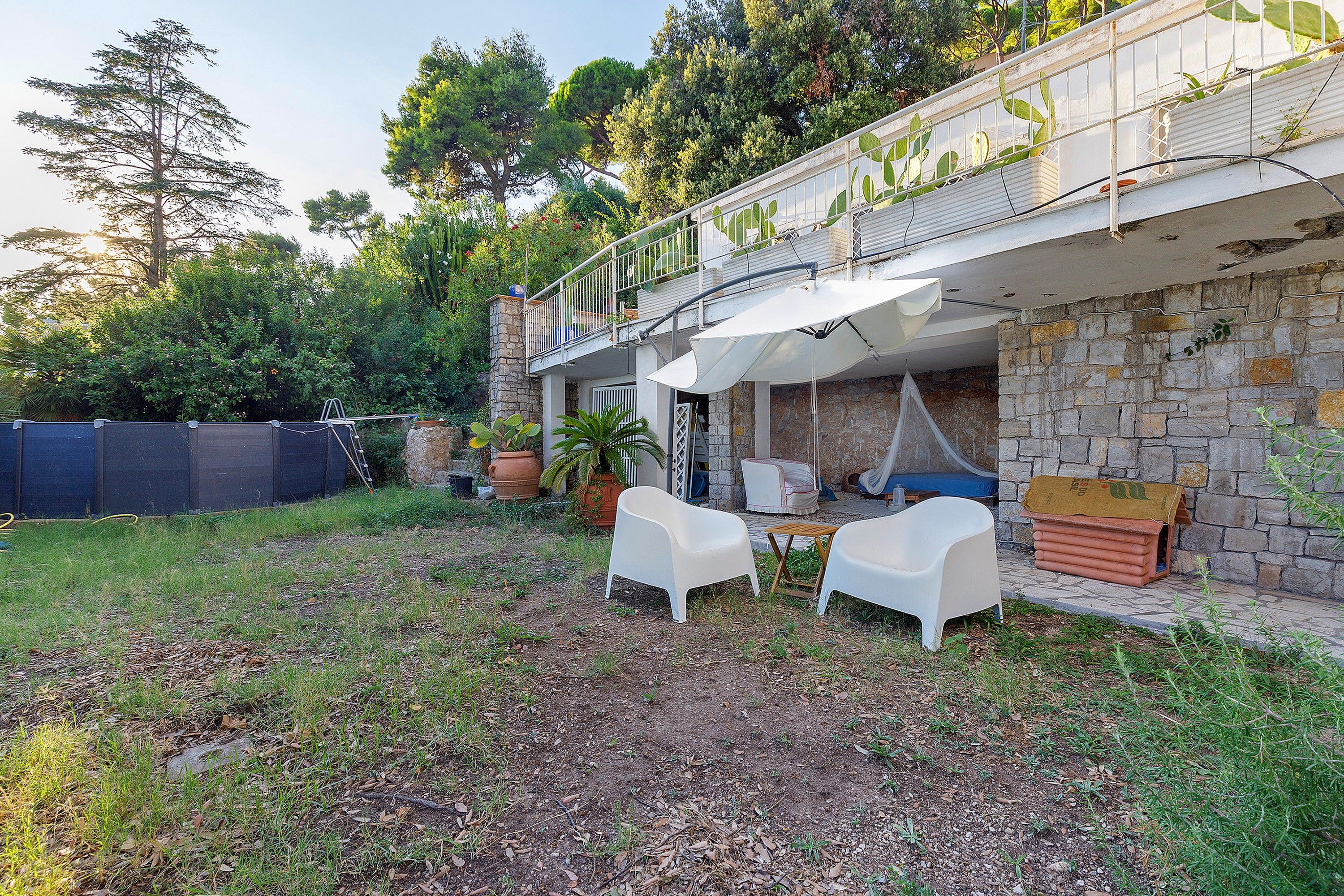 A patio with two white chairs, a table, and a hanging chair. There is a stone wall and a metal fence in the background.