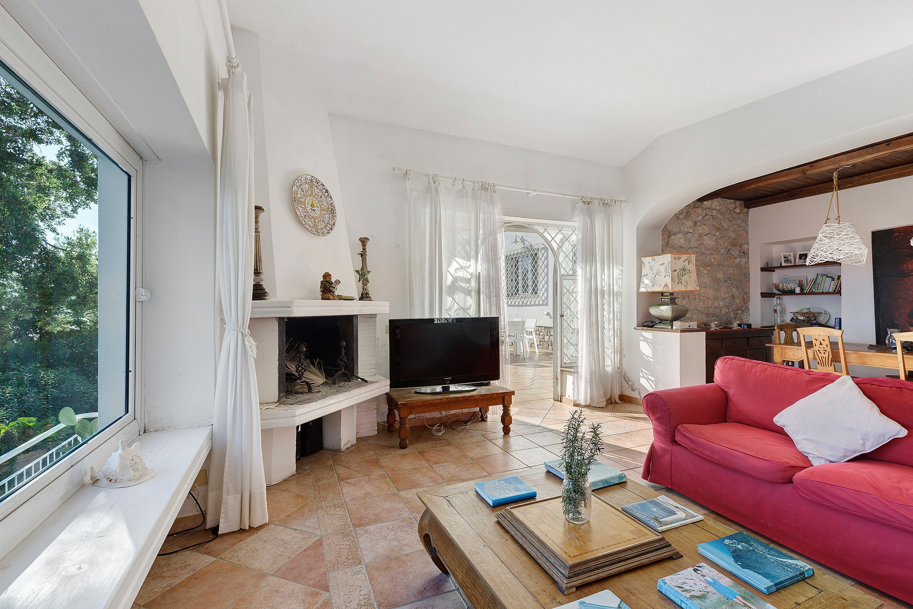 A living room with a fireplace, television, red sofa, and a dining area with a stone wall.