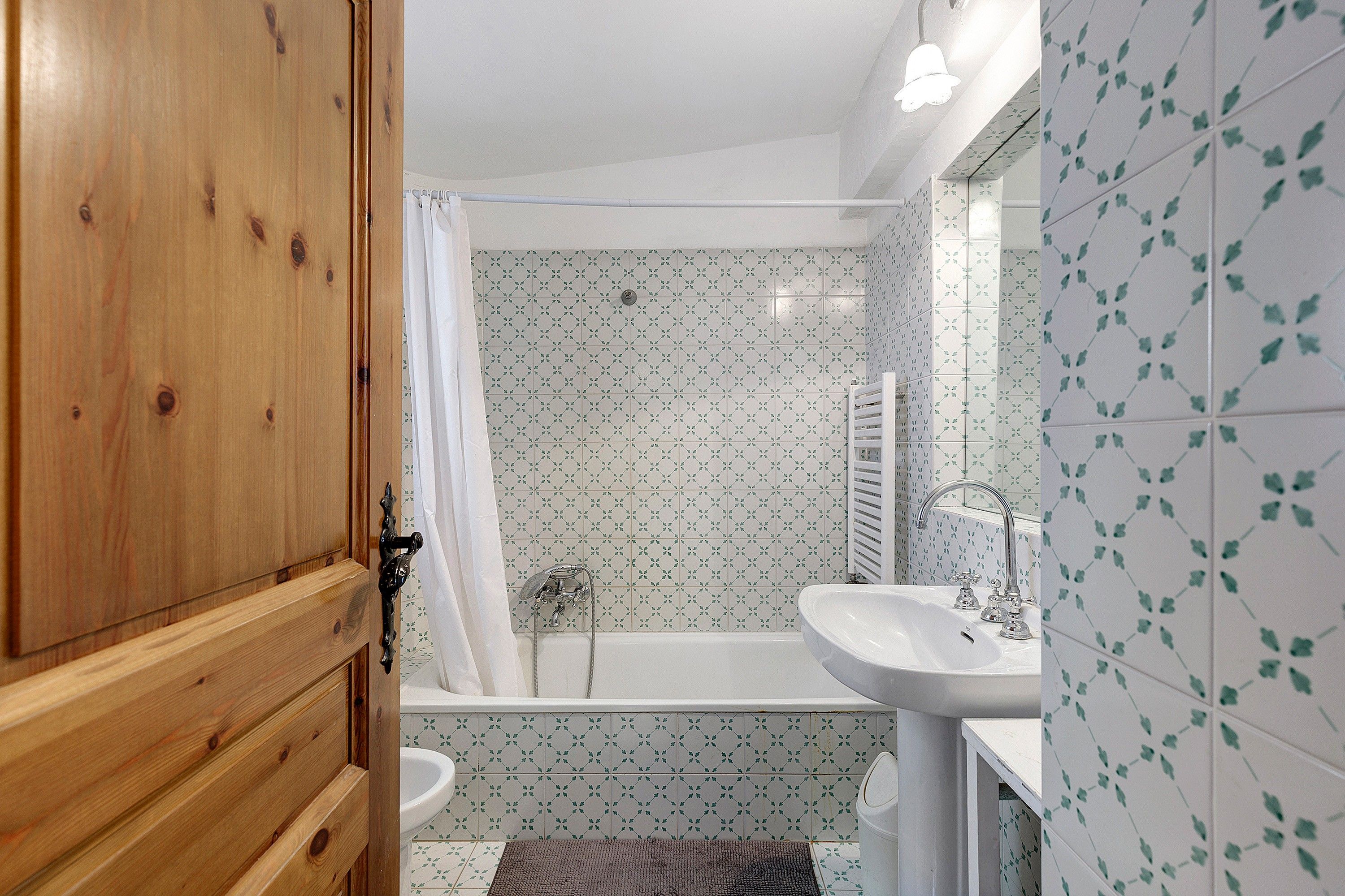 A bathroom with a wooden door, a shower with a curtain, a bathtub, and a sink.