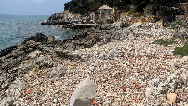 A rocky beach with a small building, a rocky shoreline, and a clear sky.