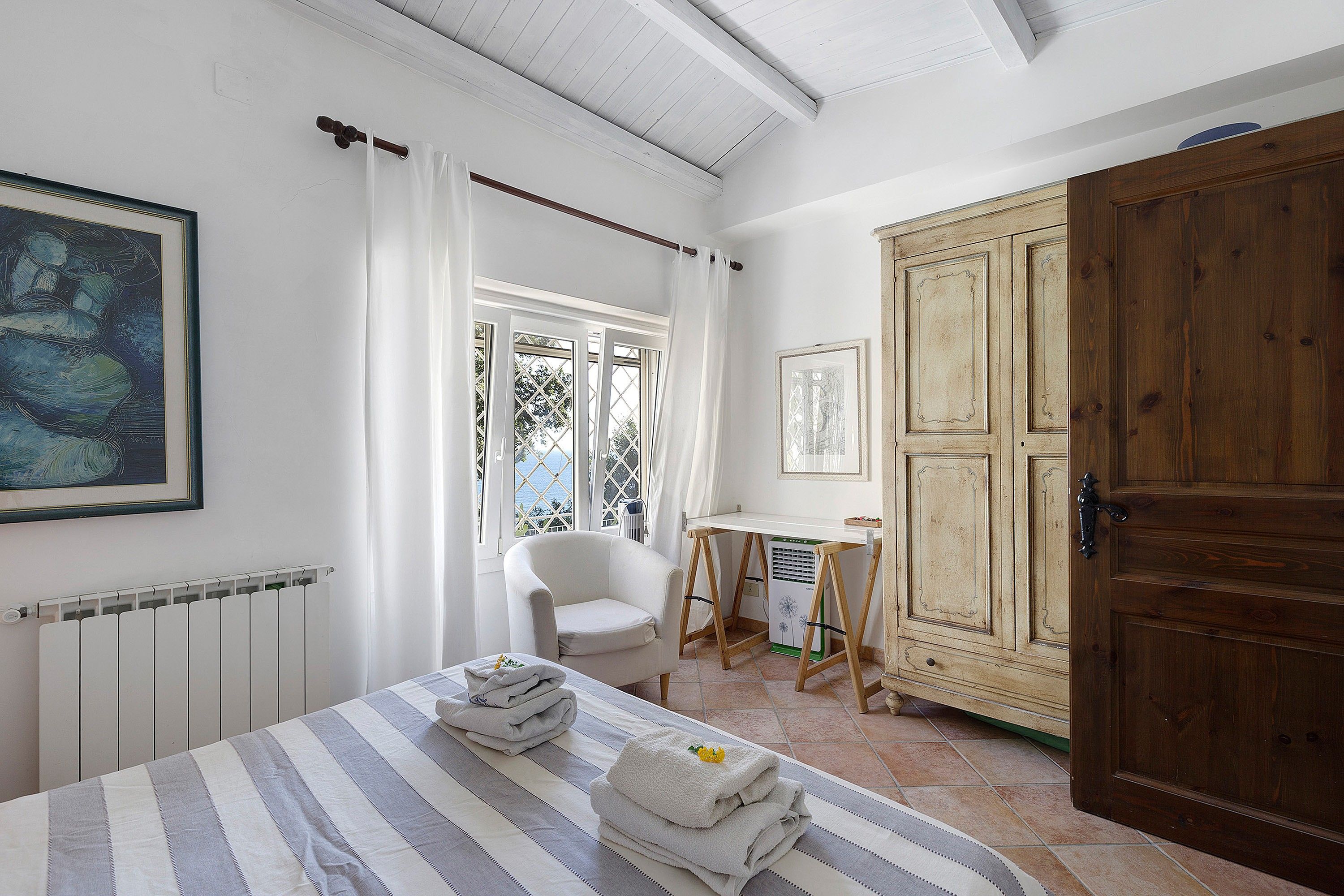 A room with a bed, a chair, a radiator, a wooden wardrobe, and a window with curtains.