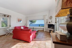 A living room with a red sofa, a fireplace, and a view of the sea.