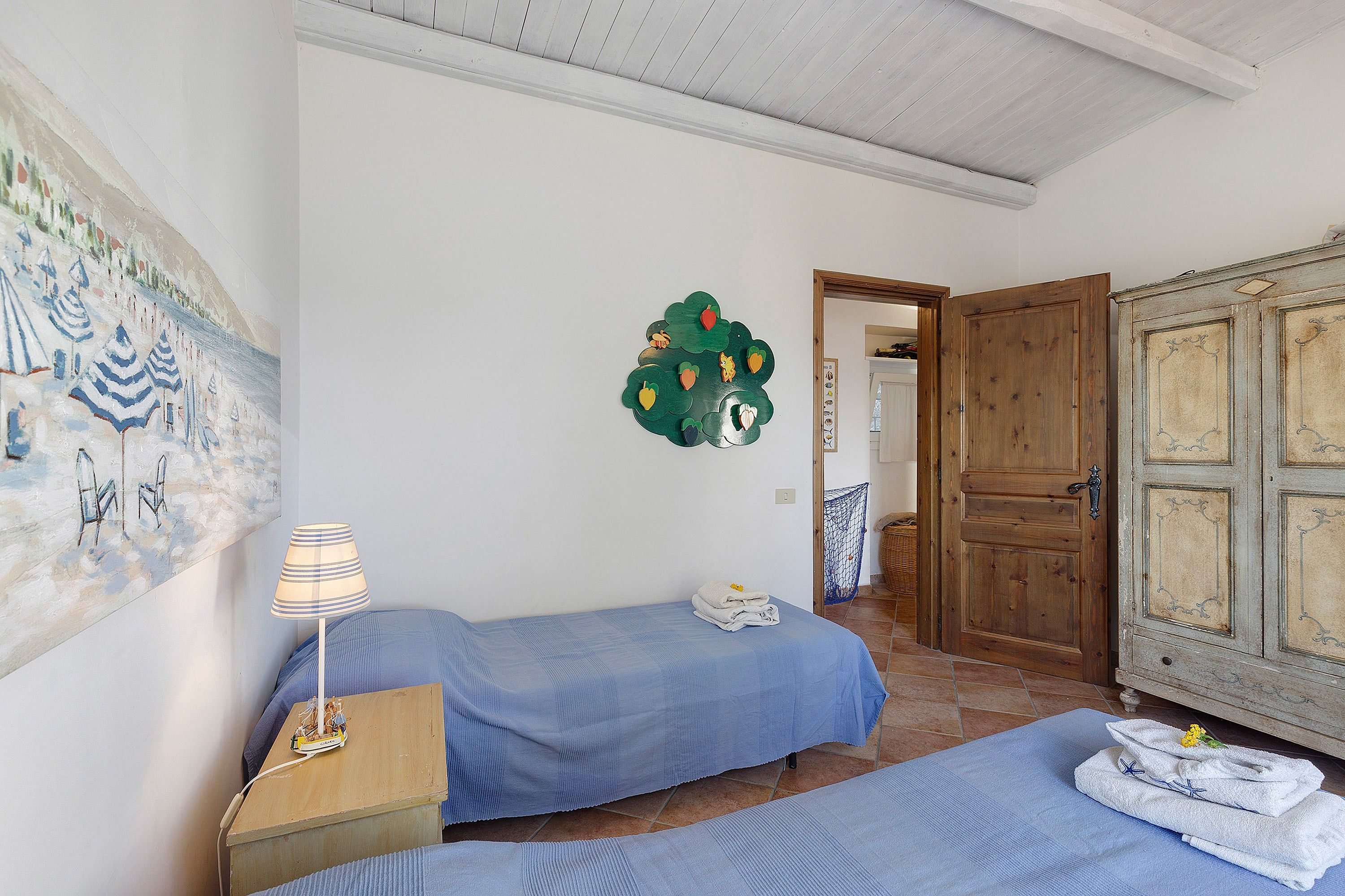 A room with two beds, a lamp, a painting, and a door.