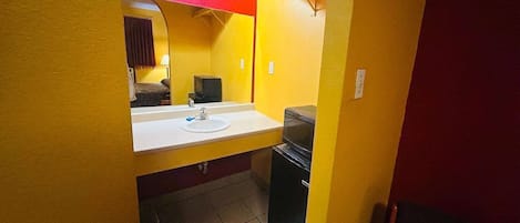 A small bathroom with a white sink, a mirror, and a black trash bin.