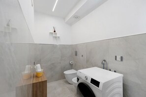 A modern bathroom with a built-in washing machine, a toilet, and a shower area.
