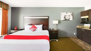 Een hotelkamer met een bed, nachtkastje, lamp, schilderij en een kitchenette.