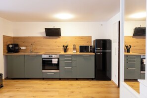 Eine moderne Küche mit grauen Schränken, einer Holz Arbeitsplatte, einem schwarzen Kühlschrank und einer Kaffeemaschine.