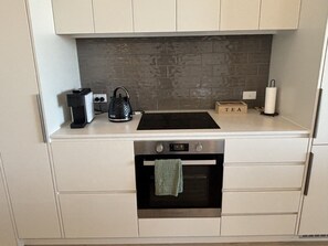 A kitchen with a built-in oven, a coffee machine, and a tea set on the counter. - Stylish CBD Escape | Sleeps 6 | Pool,Gym & Parking (Adelaide)