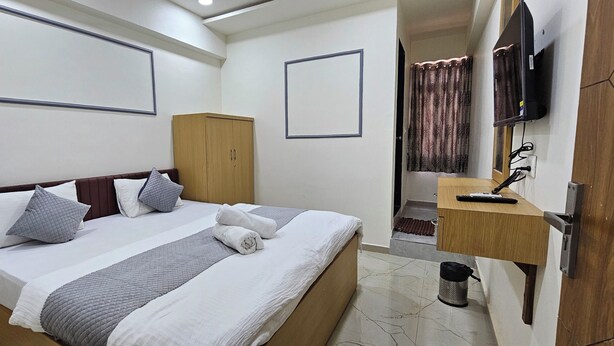 A hotel room with a bed, a wardrobe, a television, and a desk with a chair.