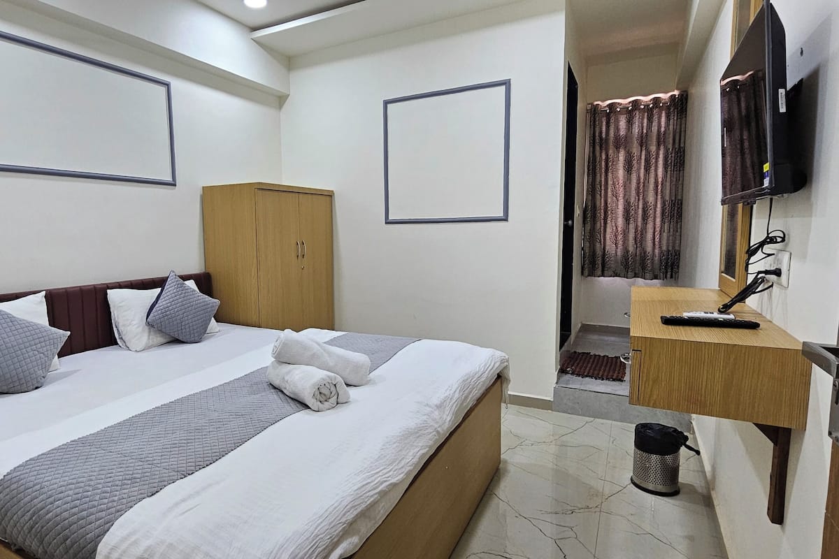 A hotel room with a bed, a wardrobe, a television, and a desk with a chair.