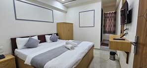 Quarto de hotel com cama, guarda-roupa, televisão e secretária com cadeira.