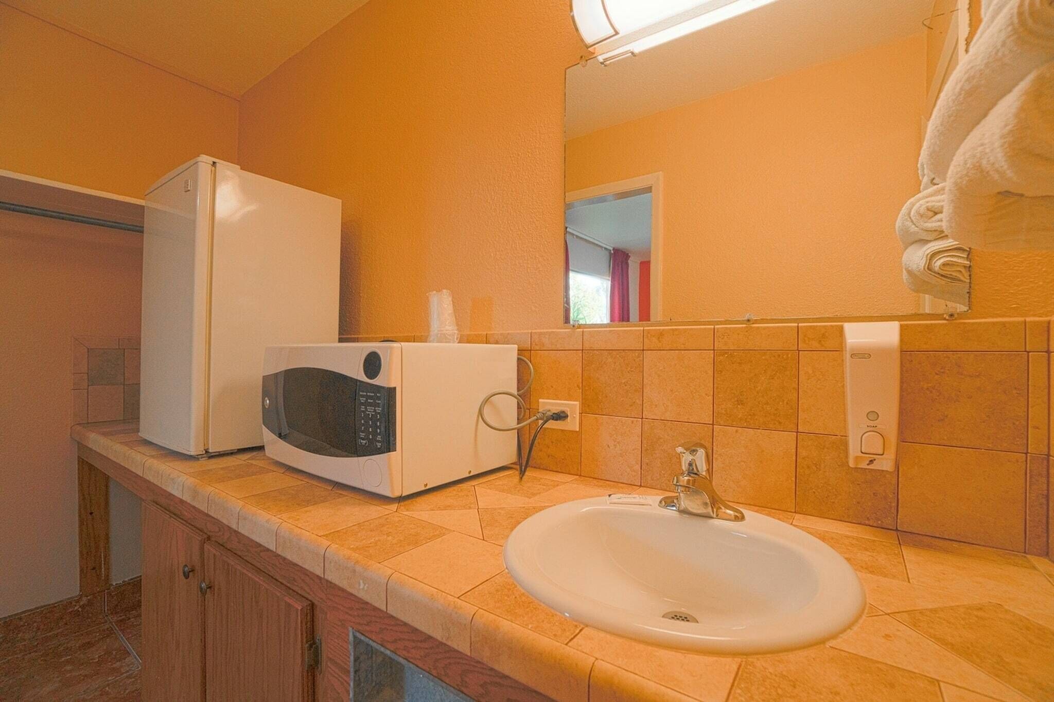 Ein Badezimmer mit Waschbecken, einer Mikrowelle, einem Kühlschrank und einem Spiegel.