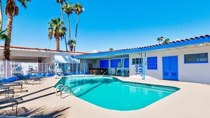 A pool area with a clear blue pool, sun loungers, and palm trees.