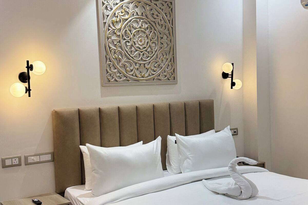 Una moderna camera d'hotel con un letto grande, un comodino, una lampada a parete e una ventola a soffitto.