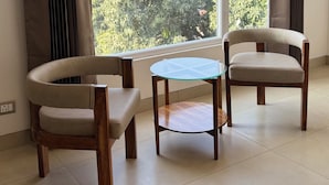 Una habitació amb dues cadires, una taula rodona petita i una finestra gran amb cortines.