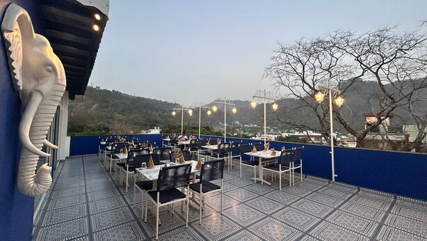 Un restaurant a l'aire lliure amb taules i cadires, una escultura decorativa d'elefant i vista a les colines.