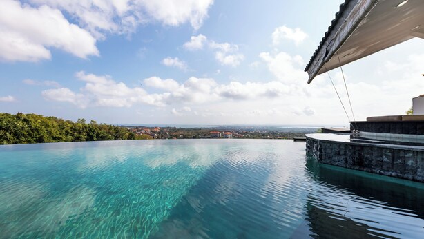 A clear infinity pool with a view of a distant town and mountains. - Villa Ocean's Height By Fays Hospitality (Bali)
