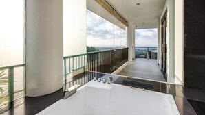 A modern hotel balcony with a large bathtub, glass railings, and a view of the city. - Villa Ocean's Height By Fays Hospitality (Bali)