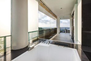A modern hotel balcony with a large bathtub, glass railings, and a view of the city. - Villa Ocean's Height By Fays Hospitality (Bali)