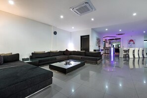 A modern living room with a sectional sofa, a coffee table, and a dining area with chairs. - Villa Ocean's Height By Fays Hospitality (Bali)