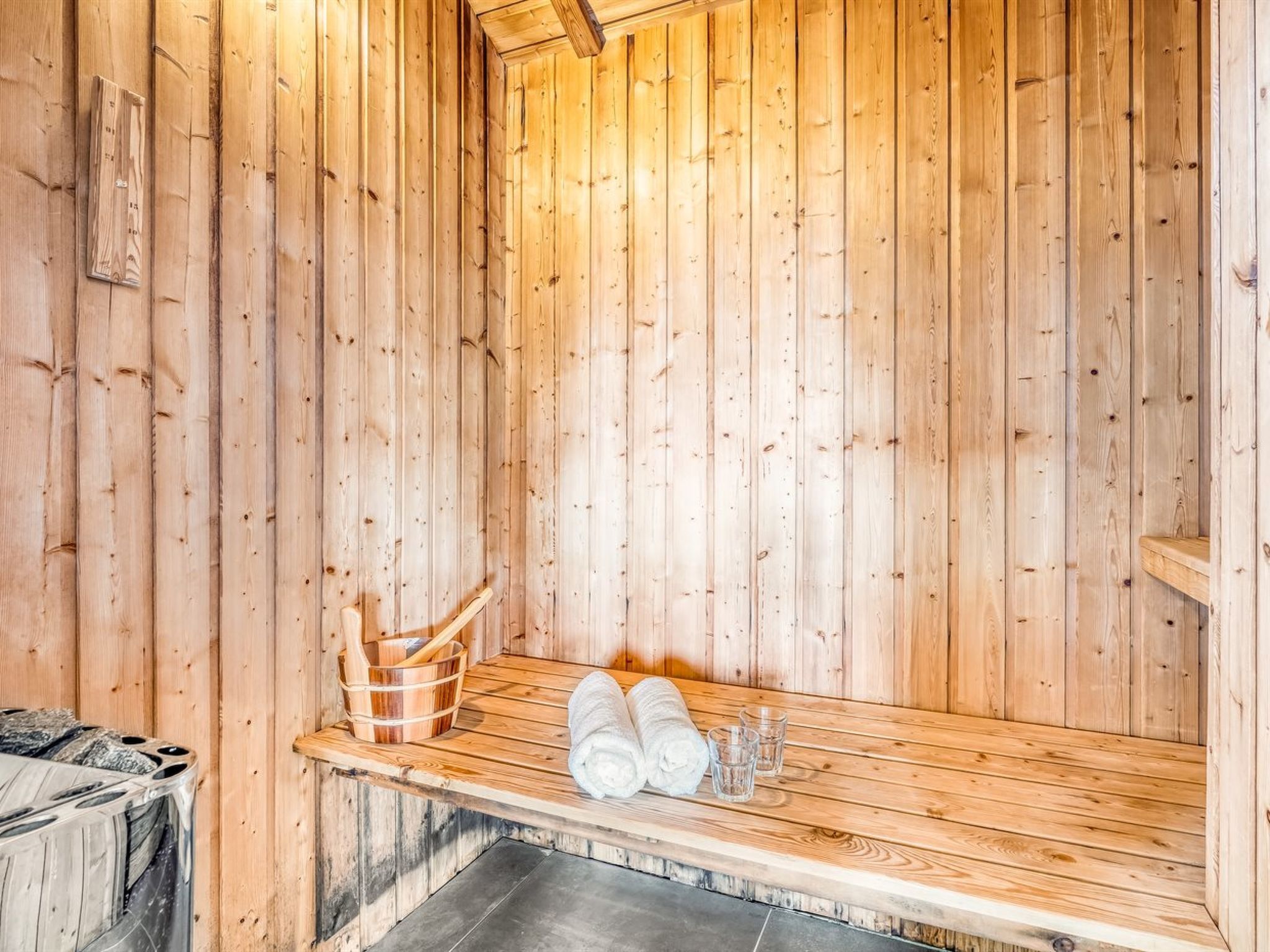 Een sauna met houten wanden, een bankje, een houten emmer en handdoeken.