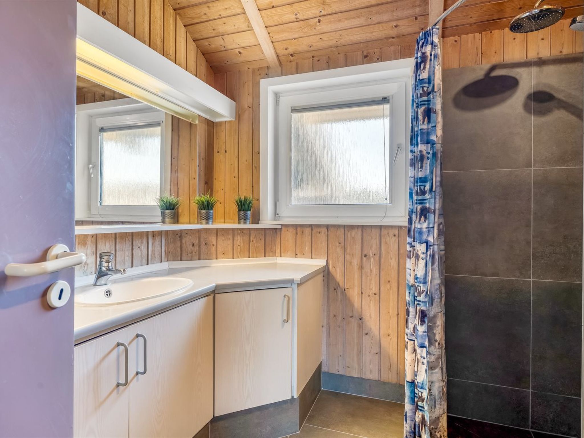 Une salle de bain avec des murs en bois, une douche, un lavabo et un miroir.