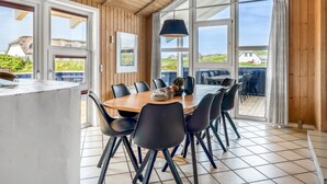 Un espace repas doté d’un plafond en bois, de grandes fenêtres et offrant une vue sur le paysage.