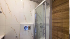 A modern bathroom with a glass-enclosed shower, marble walls, and wooden flooring. - 15 - Alexandros Apartments by SDR (Paralia)