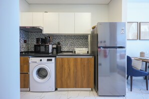 A compact kitchen with a washing machine, a refrigerator, and wooden cabinets. - Bloomfields Studio - The Gate Masdar (Abu Dhabi)