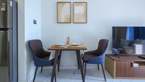 A modern kitchen with a built-in refrigerator, a dining table with two chairs, and a television on a wooden stand. - Bloomfields Studio - The Gate Masdar (Abu Dhabi)