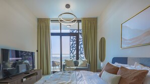 A hotel room with a bed, a TV, a sofa, and a large window. - Bloomfields Studio - The Gate Masdar (Abu Dhabi)