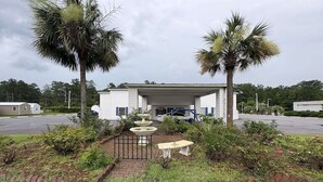 A building with a covered entrance, a fountain, and palm trees.