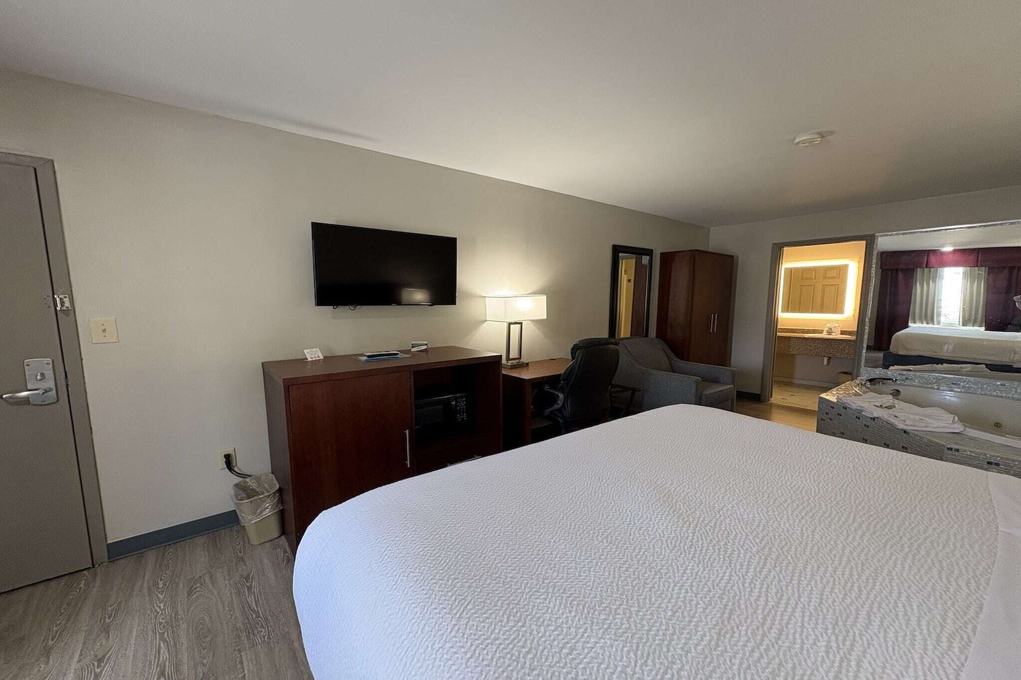 A hotel room with a large bed, a desk with a chair, a television mounted on the wall, a lamp, and a wardrobe.